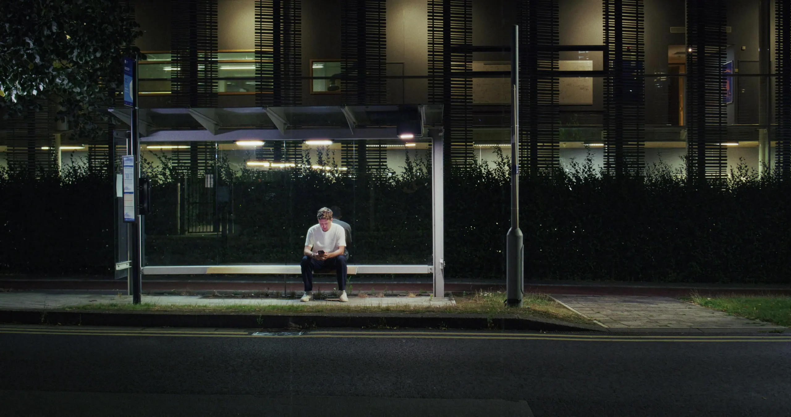 Mark G Smith waits alone in a lit bus shelter at night
