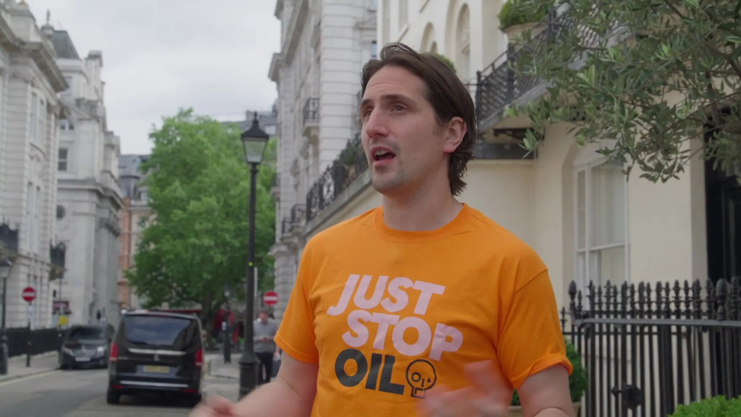 Luke McQueen as Graham, in a Just Stop Oil T-shirt, talking on a London street