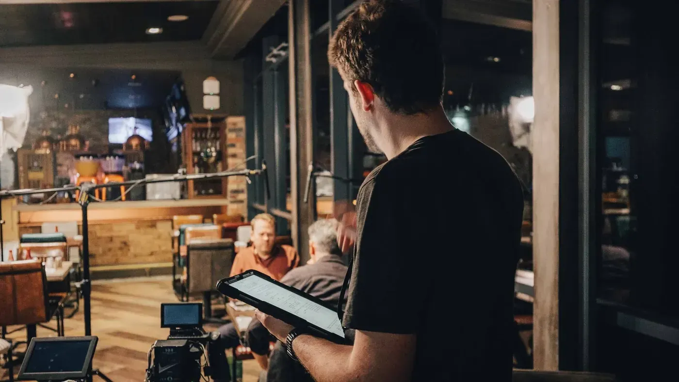Alex Stockley checks a tablet beside the camera, with Toby Williams and David Mills at the table