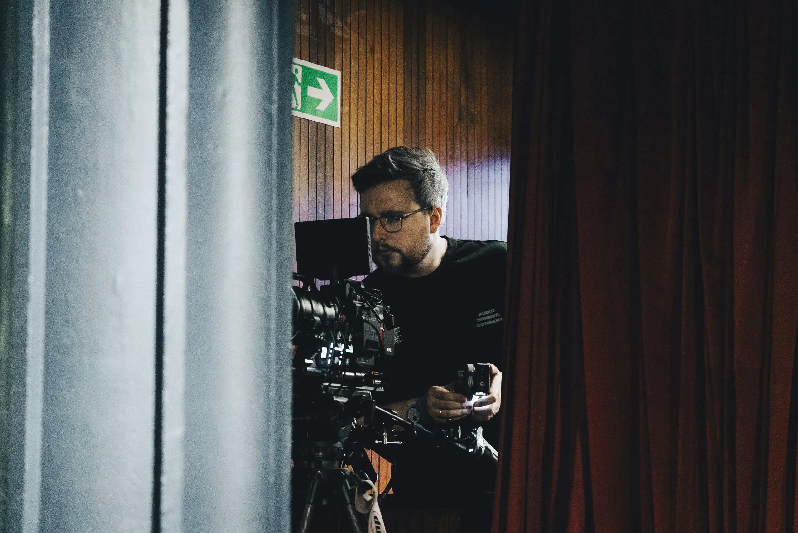 Lewis Rees operating camera in the wings beside the curtain